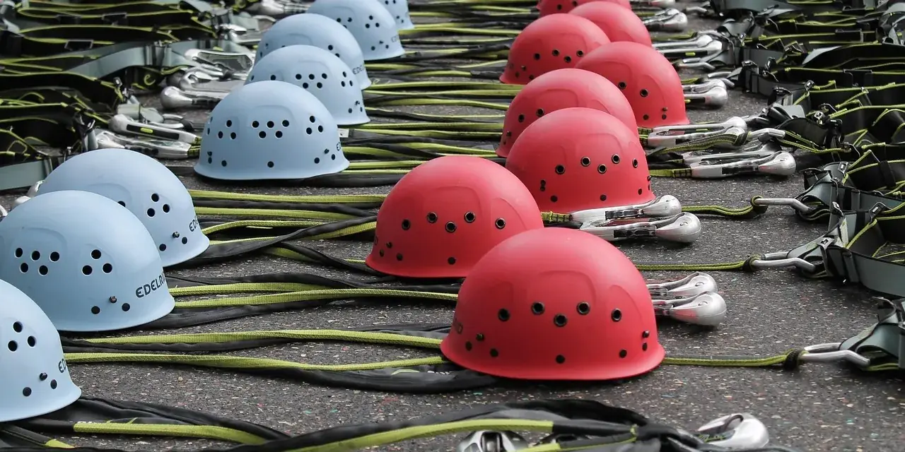 Casques d’escalade bleus et rouges et baudriers alignés au sol avant une activité de groupe
